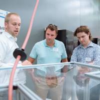 A student explaining an automatic drill bit straightener to guests at the Engineering Design Project Preview